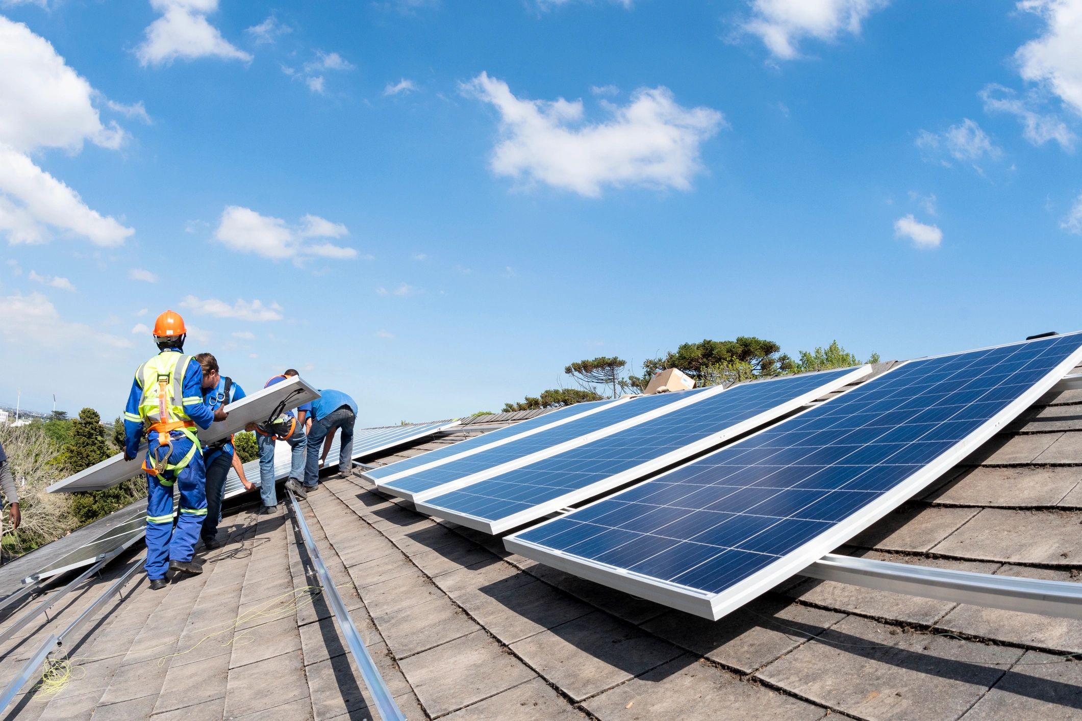 Wide shot men moving solar panel on roof